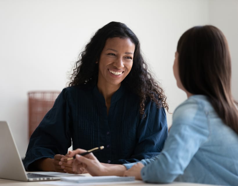 Two women sitting in front of laptop in office setting having discussion. 
