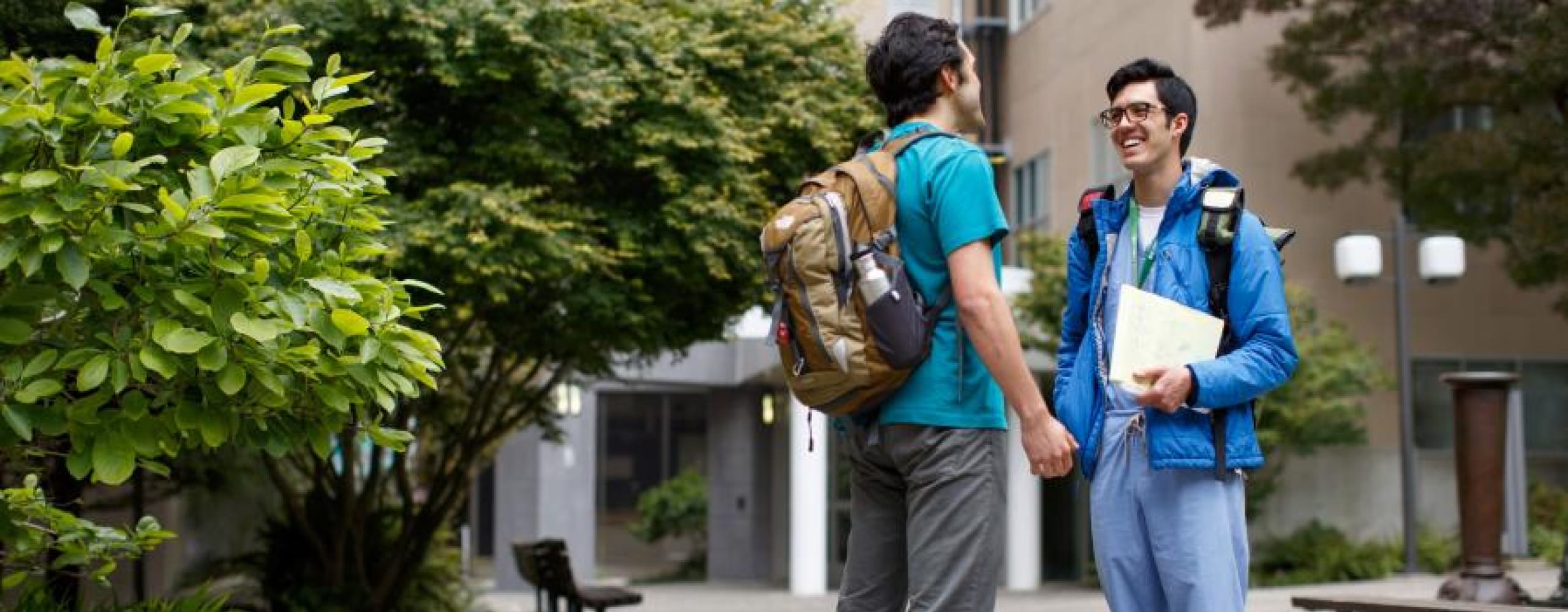 Two male students with backpacks talking and laughing outside on a campus.