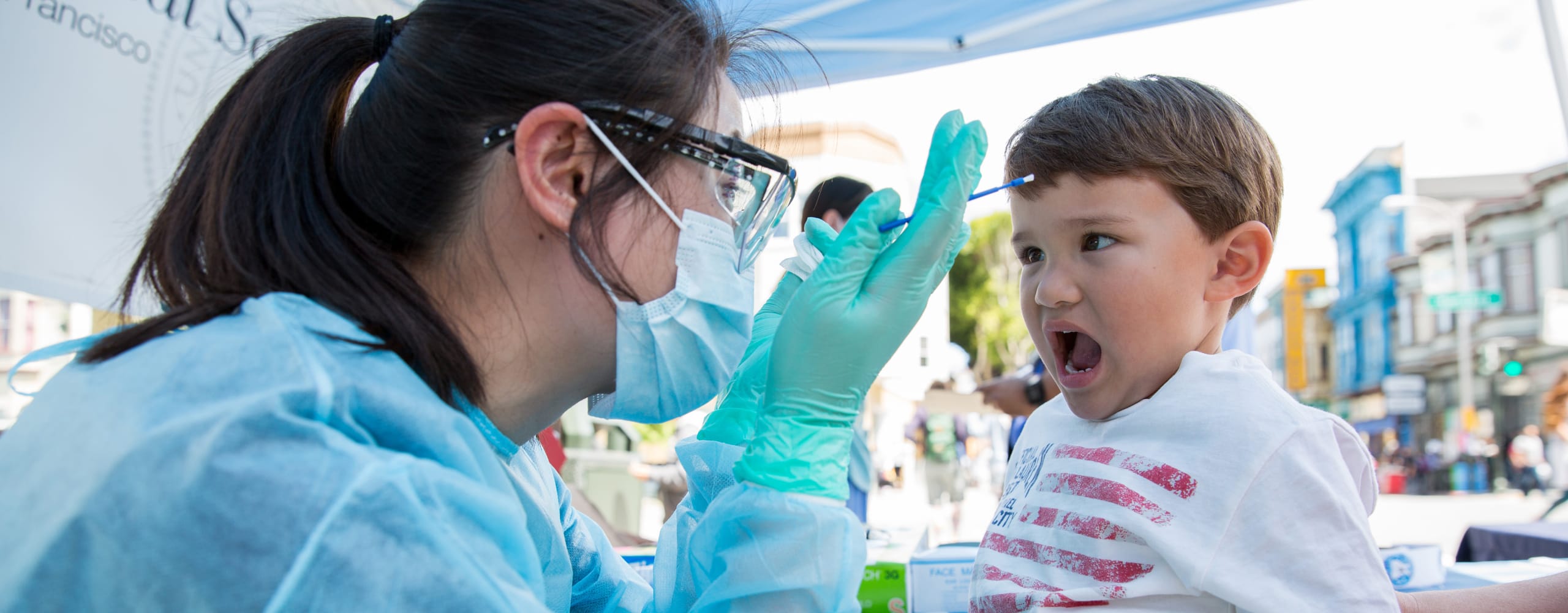 Child receiving a medical swab test at an outdoor clinic.