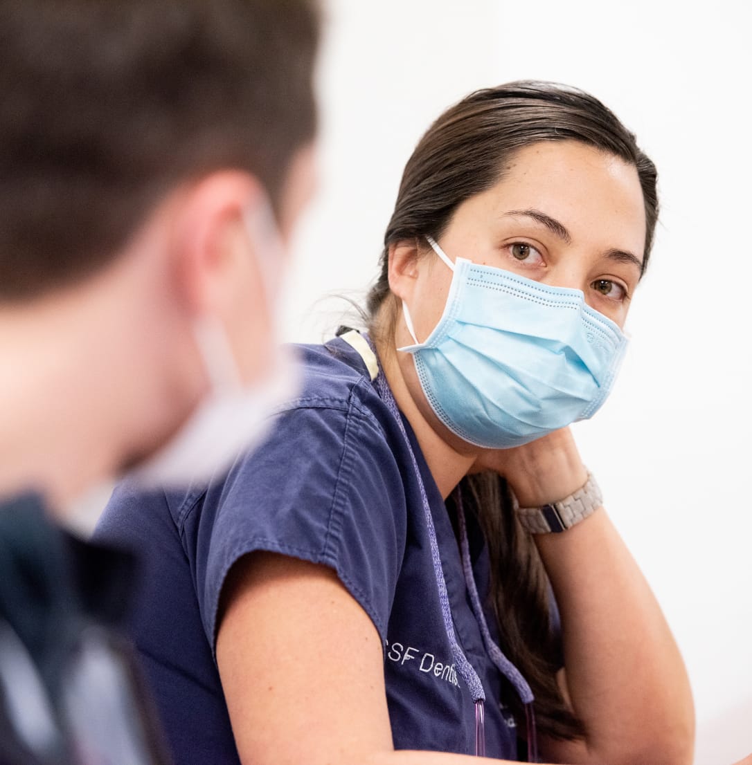 Healthcare professional in blue scrubs and face mask.