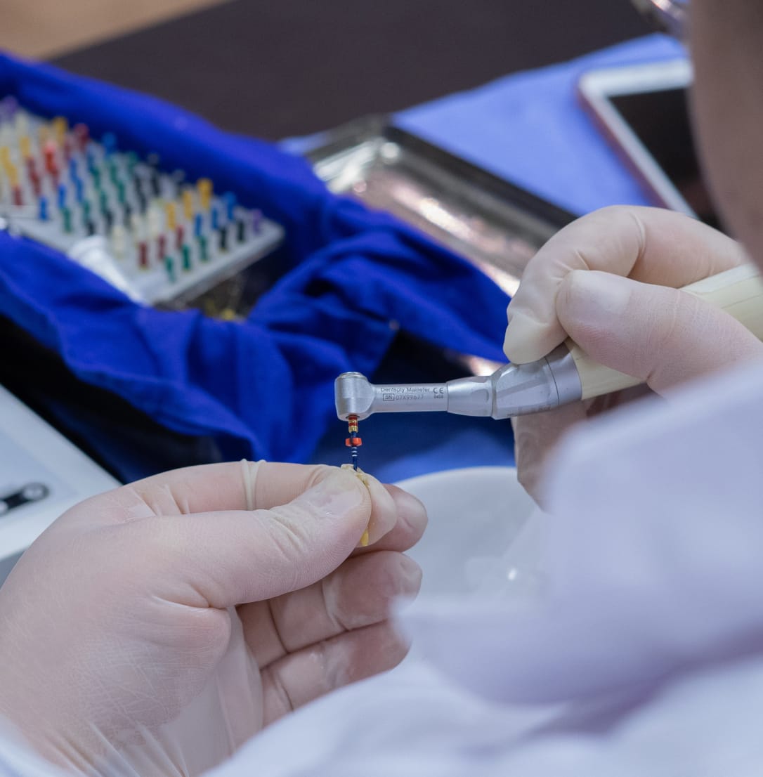 Gloved hands using a dental handpiece to work on a small endodontic component.