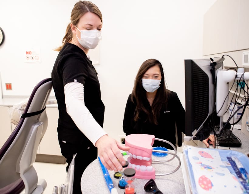 Dental professionals in black scrubs with a tooth model and sand timers.
