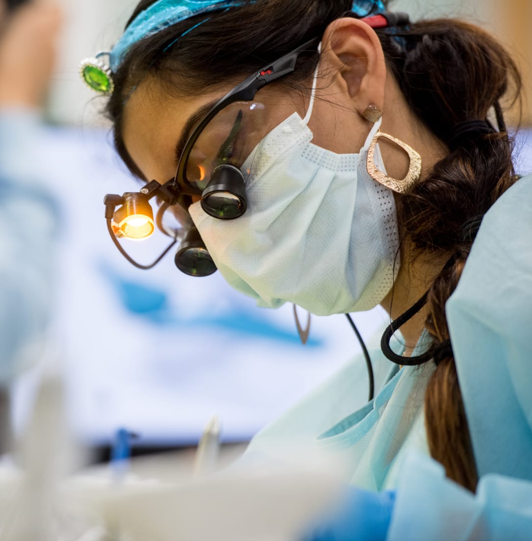 A dental professional wearing a mask, magnifying loupes, and a bright headlight focused on a task.