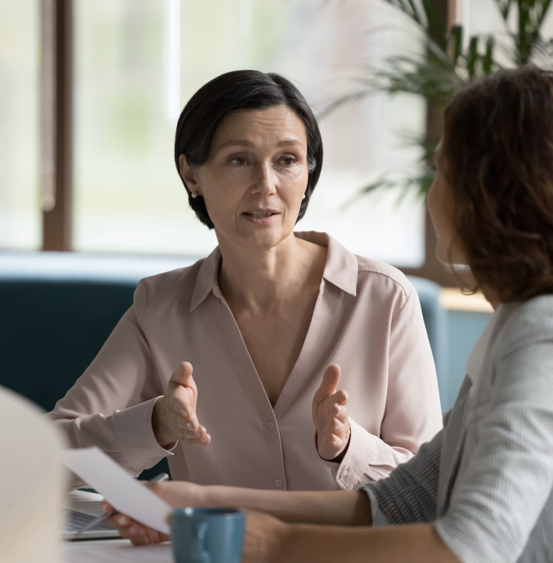 Two women having conversation while seated at a table in an office setting. 