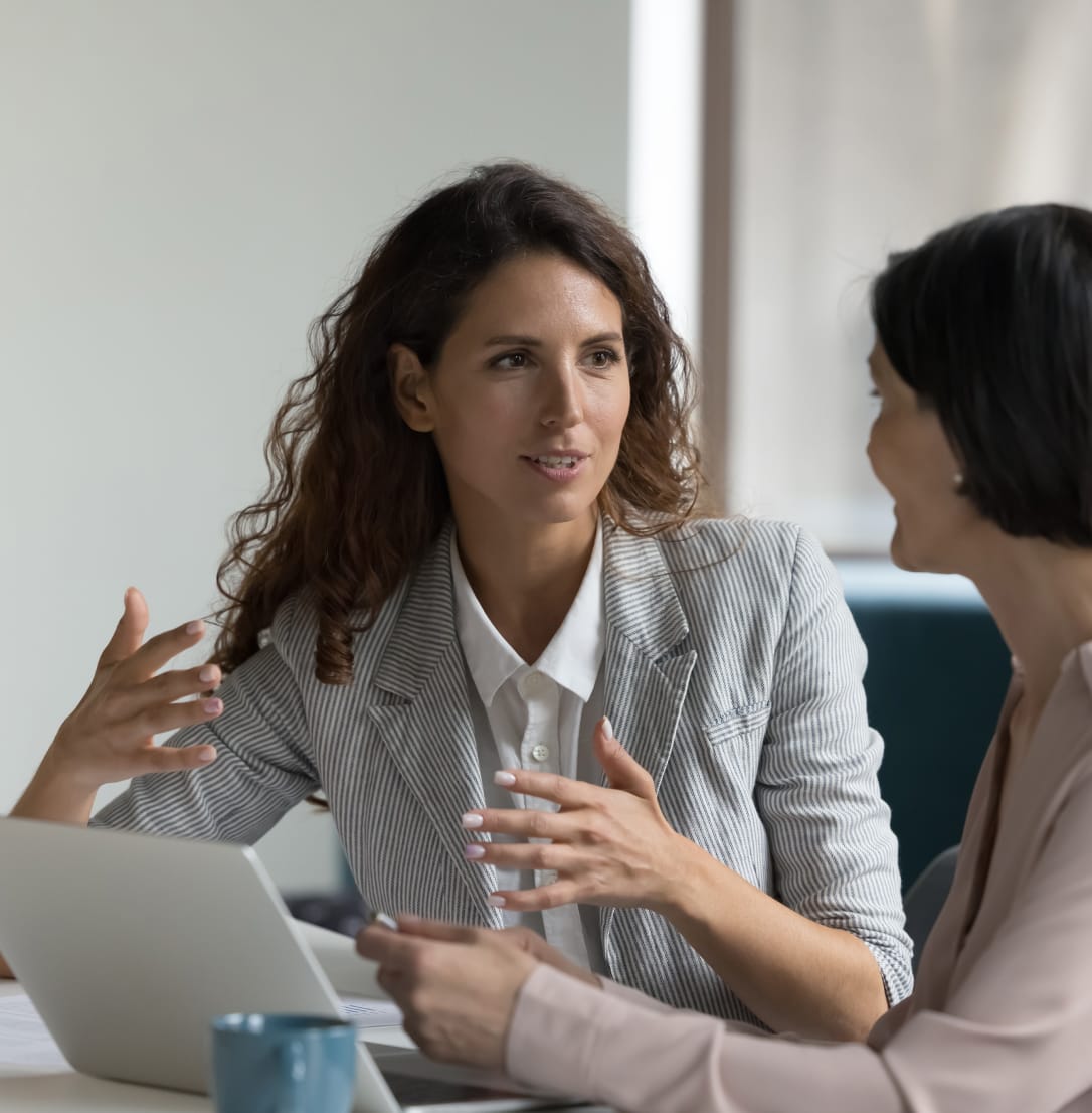 Two women sitting in front of laptop in office setting having discussion. 